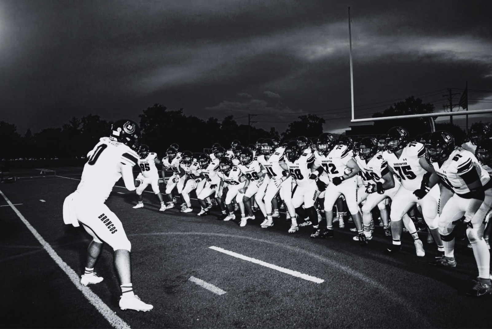 High school football team charging onto the field under stadium lights